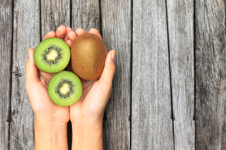 Hand holding half kiwi fruits on wooden table backgroundの写真素材