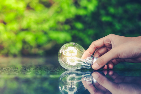Energy saving concept. Hand holding light bulb on abstract nature background.の写真素材