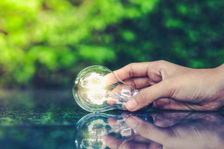 Energy saving concept. Hand holding light bulb on abstract nature background.の写真素材