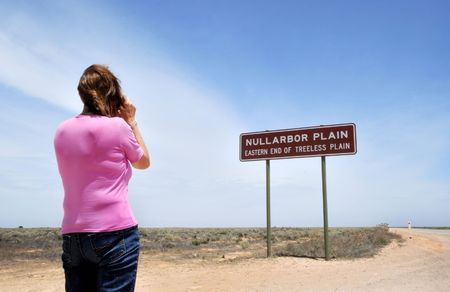 Girl taking photo of the sign on the Eyre Highway, Nullarbor Plain,of Treeless Plain, South Australiaの写真素材