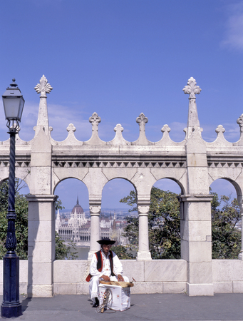 BUDAPEST,HUNGARY-NOVEMBER 11,2008: Parliament view through Fishermans Bastion with music player in traditional costume at foregroundのeditorial素材