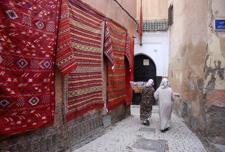MARRAKESH,MOROCCO-MARCH 05, 2009: Moroccan carpets alongside a small alley in the souk with two women with food at the end of the streetのeditorial素材