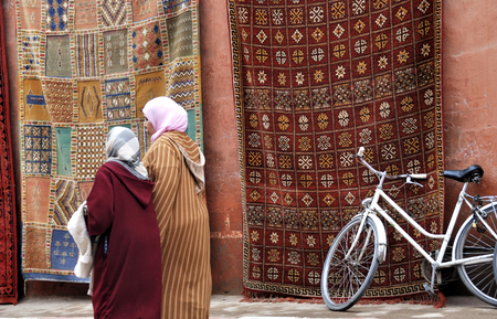 MARRAKESH,MOROCCO-MARCH 05, 2009: Moroccan carpets and a bicycle alongside a small alley in the souk with two women passing by.のeditorial素材