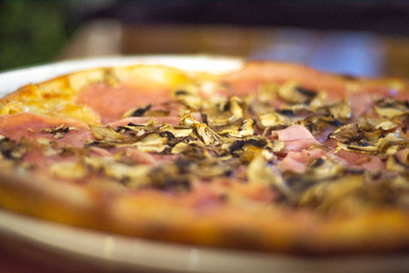 Pizza with ham, mushrooms and cheese on a wooden table.の写真素材