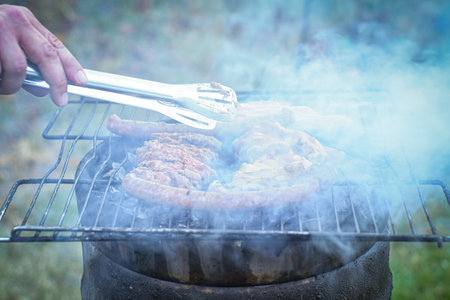 Close-up of man's hand cooking meat on barbecue grill.