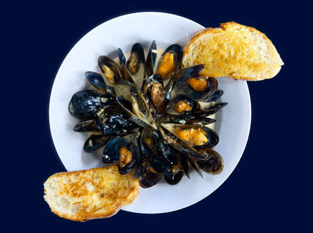 A dish of appetizing fresh mussels in white wine sauce served with toasted bread.の写真素材