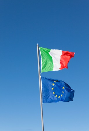 Flags of Italy and Europe waving in the wind on blue sky backgroundの写真素材
