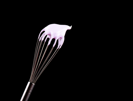 Metal whisk with pink cream isolated on black background. Clipping path.