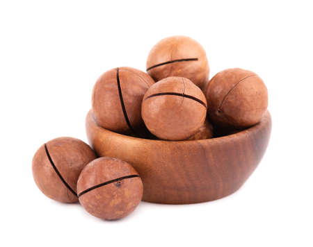 Macadamia nuts in wooden bowl, isolated on white background. Unshelled macadamia