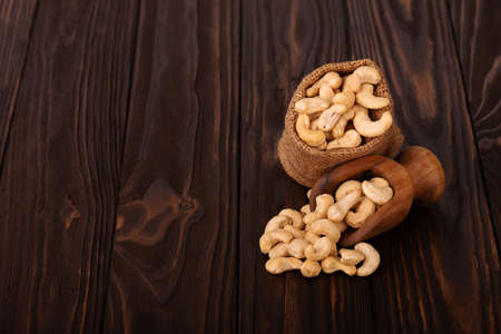 Cashew nuts in bag and wooden scoop, on wooden background. Roasted cashew nuts.の写真素材