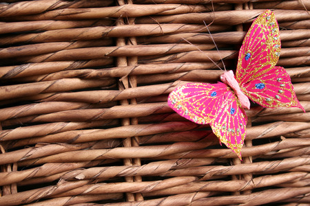 Pink butterfly decorated with glitter on a woven wood background 