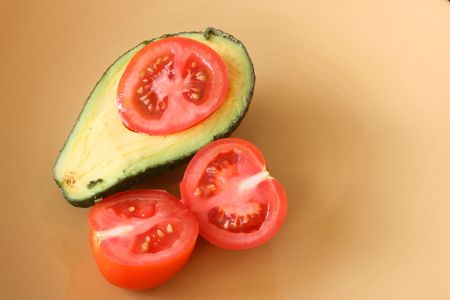 Half an Avocado and sliced tomatoes on a yellow plateの写真素材