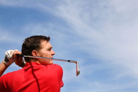 Young golfer hitting an iron against a half cloudy skyの写真素材