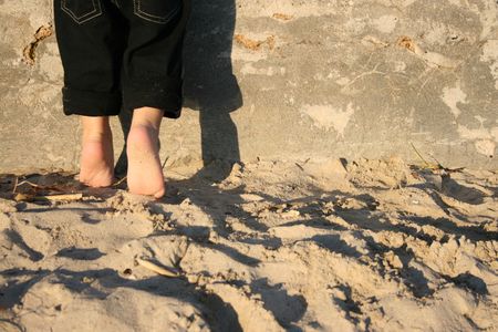 Toddler standing on the beach against a wall on his tippie toesA child's feet on the beach standing...