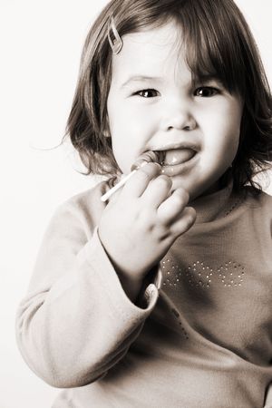 Toddler girl with chubby cheeks eating a sticky lollipopの写真素材