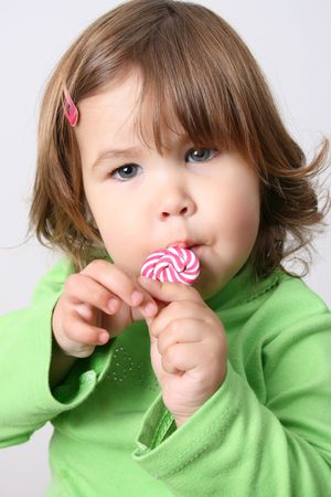 Cute brunette toddler eating lollipops wearing a green shirtの写真素材