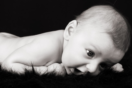 Beautiful three month old baby boy lying on black fur の写真素材