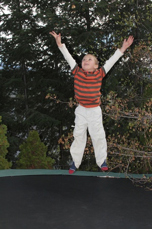 Blond boy jumping on his trampline in the gardenの写真素材