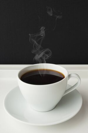 a white cup of coffee with smoke on a trayの写真素材