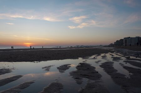 beautiful sunset in a beach scene with the silhouette of people in the background and blue and orange colorsの写真素材