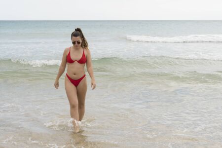 beautiful european young girl in red bikini on th beach. portrait of a woman smiling at the sea. girl in swimwear enjoying and walking on the beachの写真素材