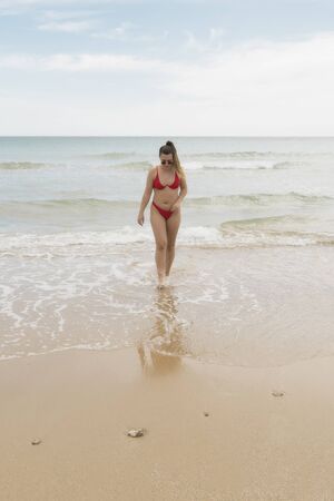 beautiful european young girl in red bikini on th beach. portrait of a woman smiling at the sea. girl in swimwear enjoying and walking on the beachの写真素材