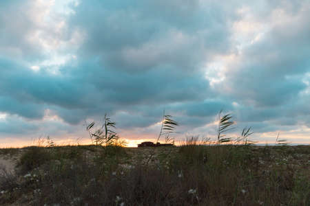 nice cloudy sunset on the beach forming a storm with the silhouette of a house in the backgroundの写真素材