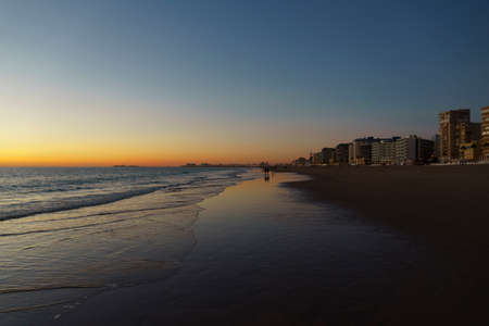 a beautiful and colorful sunset on the beach with a city in the backgroundの写真素材