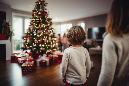 Children with their backs looking at the Christmas tree and gifts and family in the background. Concept of Christmas day or three wise men day.の素材