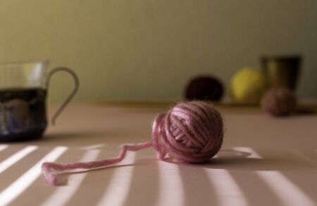 Pink ball of wool in the sun with shadows. Knitting needles and balls of yarn in the background. Room for copy.の写真素材