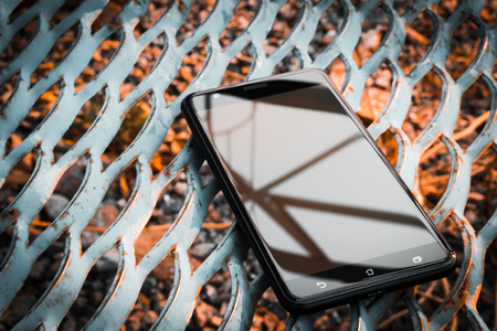 Black smartphone with beautiful reflections on the background of rusty iron latticeの写真素材