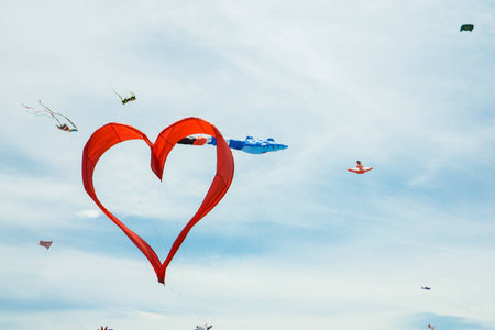 Red heart shape kite is flying in blue skyの写真素材