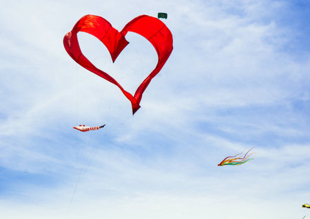 Red heart shape kite is flying in blue skyの写真素材