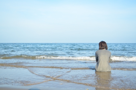 the girl is sitting alone at the beach and looking through the seaの写真素材