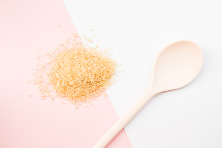 Heap of granulated brown sugar on pink and white background with soft pink spoon.