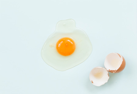 Top view of raw egg with eggshell on soft blue background.の写真素材