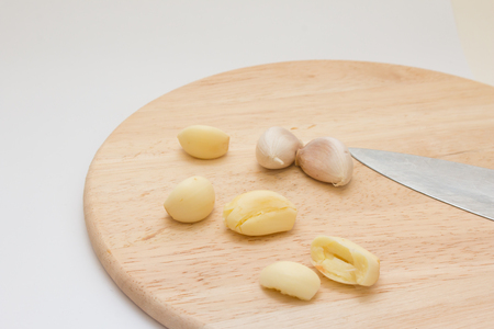 Peeled garlic on wooden chopping block on white background.の写真素材