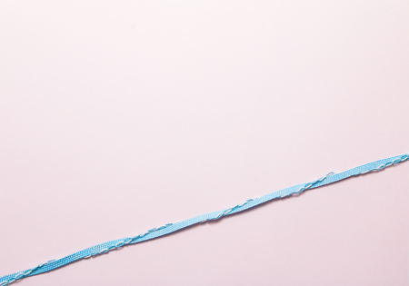 Blue ribbon on soft pink paper background.の写真素材