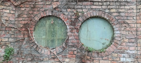 Two round windows with very old glass, brick wall.の写真素材
