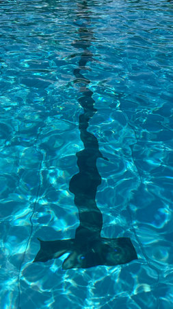 Vertical photo of T-mark in deep blue rippling water in swimming pool with sun reflection.