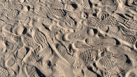 Multiple footprints of shoes on sandy beach. Various sole patterns.