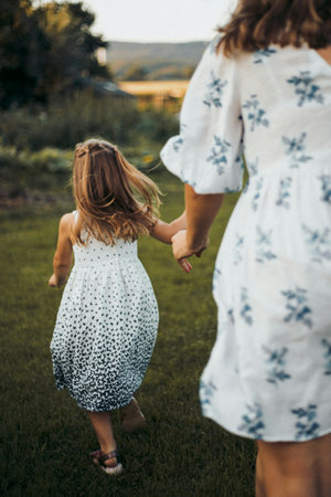 Back view of mother and daughter holding hands while walking in the parkの写真素材