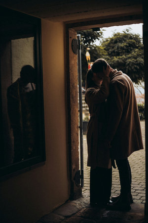 A young man in a coat stands in front of the window in the old town.の写真素材