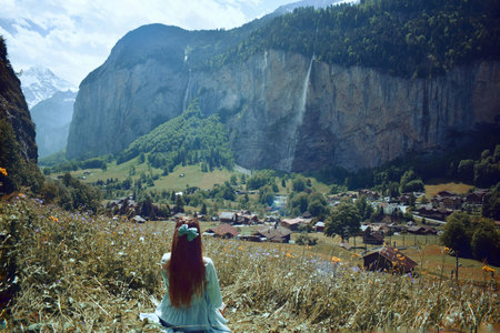 Girl sitting on a meadow in front of a waterfall in the mountainsの写真素材