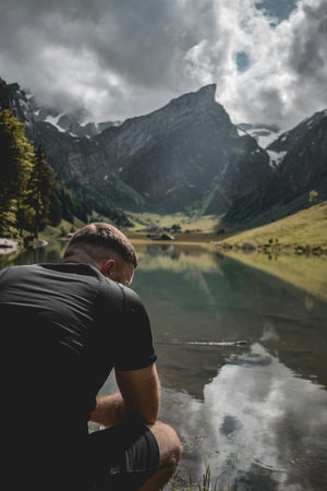 Man sitting in front of a mountain lake and looking at the mountainsの写真素材