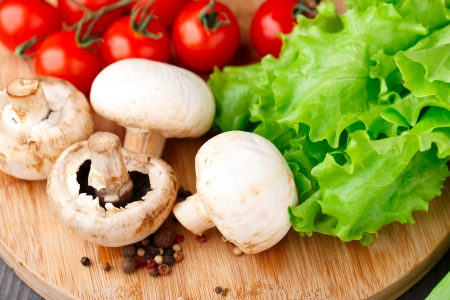 Mushrooms, tomato, lattuce and pepper on a wooden boardの写真素材
