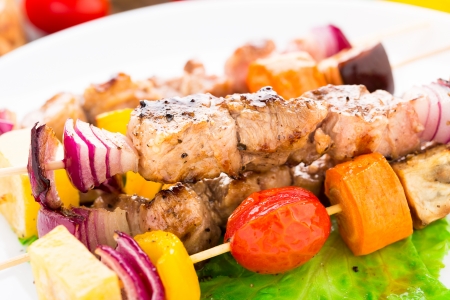 Barbecued pork and vegetable kebabs on a plateの写真素材