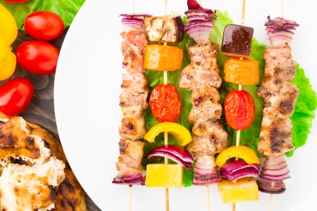 Barbecued pork and vegetable kebabs on a plateの写真素材