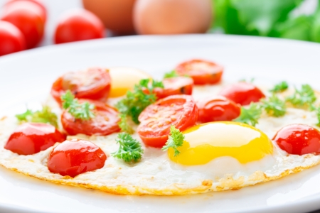 Fried eggs with cherry tomatoes on a plateの写真素材