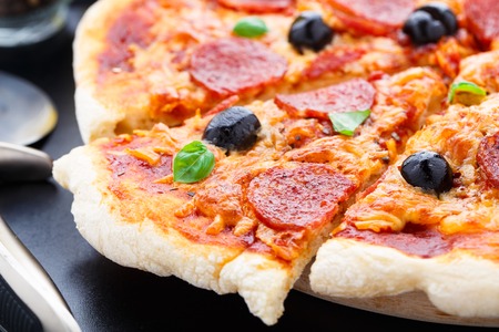 Delicious pepperoni pizza with olives on a black table.の写真素材